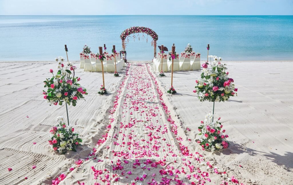 Beach wedding venue settings decorating with red and pink flowers, roses petals on the aisle