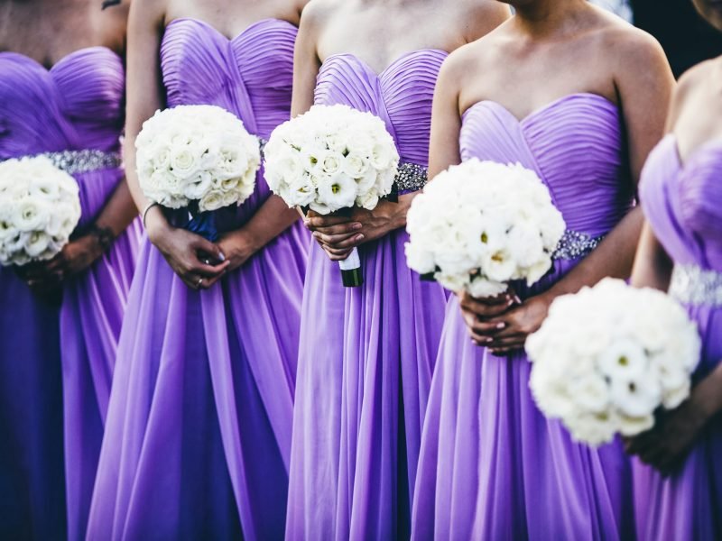 Wedding ceremony with bridesmaids wearing purple dresses and holding white flowers.